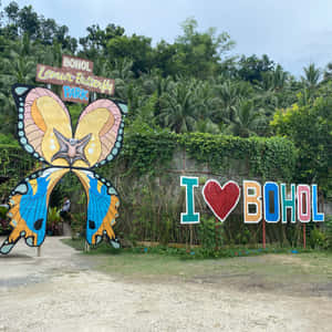 熱帶公園入口處色彩繽紛的蝴蝶拱門和 I heart Bohol 標誌。 — 美麗蝴蝶 壁紙