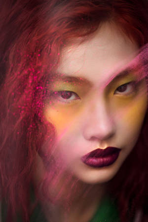 一位擁有紅髮和誇張妝容的女性，在色彩繽紛的發光光效下。