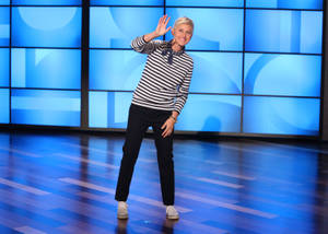Ellen DeGeneres 在藍色燈光的電視攝影棚舞台上揮手。