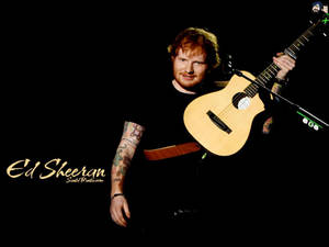 Ed Sheeran 在黑色背景前抱著一把木結他，紋身清晰可見。