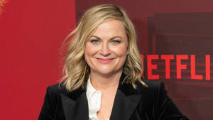 穿著黑色西裝外套的女性在紅色Netflix背景下對著鏡頭微笑。