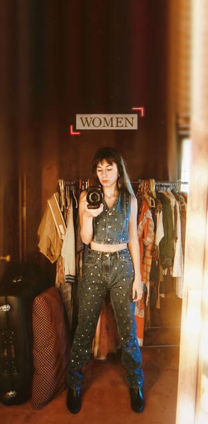 穿著牛仔布服裝的女性在服裝店內對著鏡子自拍。