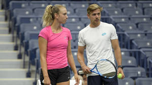 兩名網球選手在球場上手持球拍和球，身後是空的座位。 — 網球 壁紙