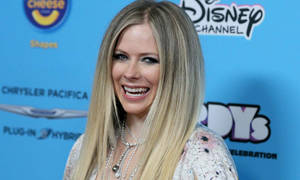 Avril Lavigne 在迪士尼頻道活動中微笑，身後有贊助商標誌。