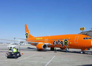 橙色Mango Airlines飛機喺機場閘口，有地勤人員同手推車。 — 藍天 壁紙