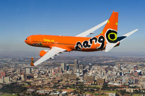橙色Mango Airlines飛機在陽光明媚的日子飛越城市。