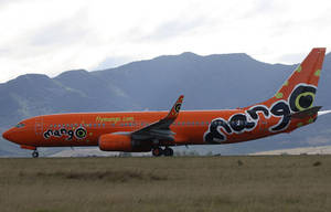橙色Mango Airlines飛機在草地上，背後有山脈
