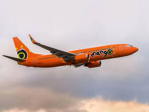 橙色Mango Airlines飛機在多雲的夕陽天空下飛行。