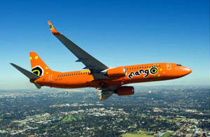 橙色Mango Airlines飛機在白天飛越城市上空。