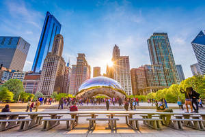 芝加哥的 Cloud Gate 雕塑反射著日落和城市天際線，周圍有人群。