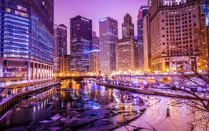 夜晚的城市天際線，燈火通明的建築物倒映在結冰的河流中。