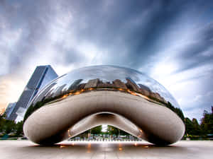 鉻合金豆雕塑在黃昏時分反射城市天際線，伴隨著戲劇性的雲彩。