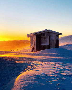 冬季風景中，日出時分一座被雪覆蓋的小木屋。
