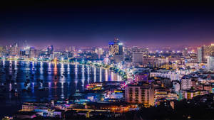 夜晚燈火通明的城市，建築物和燈光倒映在水面上。 — 極光 壁紙
