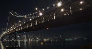 夜晚亮燈的吊橋，城市燈光倒映在水面上。