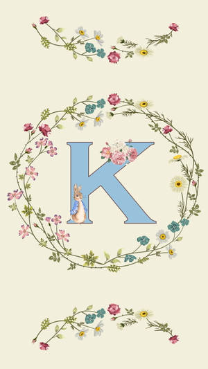 一個藍色字母K，被花環和一隻戴著藍色圍巾的兔子環繞。