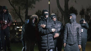 一群戴著口罩、穿著冬季外套的人夜晚站在城市公園中。