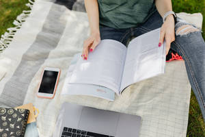 一個人在毯子上用書本、手提電腦和電話在戶外學習。