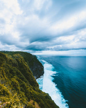 茂密的綠色懸崖在多雲的天空下與綠松石色的海浪相遇。 — 島嶼 壁紙