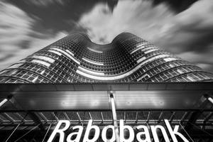 在戲劇性的多雲天空下，帶有Rabobank標誌的波浪形玻璃摩天大樓。