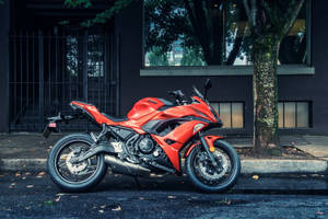 紅色Kawasaki跑車電單車泊喺行人路近樹同建築物。