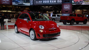 紅色Fiat 500汽車在展廳地板上展示，旁邊有其他車輛和標誌。