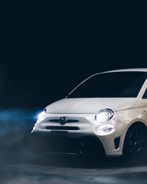 白色Fiat 500汽車在黑暗煙霧繚繞的攝影棚中發出明亮的車頭燈光芒。