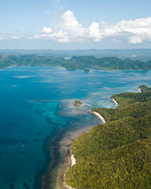 在藍天白雲下，碧綠潟湖和綠色島嶼的鳥瞰圖。