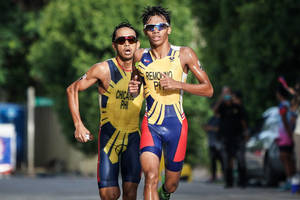 兩名男性鐵人三項運動員身穿黃、藍、紅色制服在街上比賽。 — 跑步 壁紙