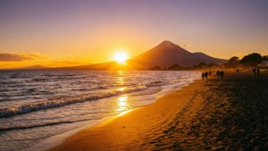 人們在金色夕陽下沿著海灘漫步，背景是山脈。