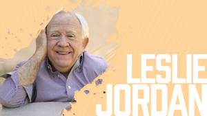 Leslie Jordan 喺橙色紋理背景前將手放喺面頰上微笑。 — Jordan 標誌 GIF 壁紙