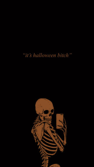 橙色骷髏拿著手機自拍，文字it's halloween bitch在黑色背景上