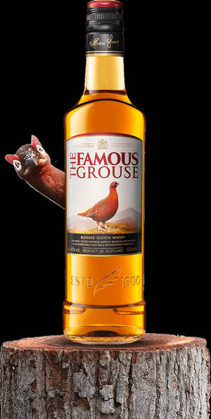 一瓶Famous Grouse威士忌放在樹樁上，一隻松雞從後面探出頭來。