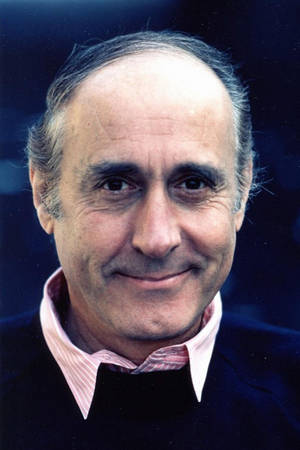 特寫肖像，一位微笑的中年男子，身穿深色毛衣和粉紅襯衫。