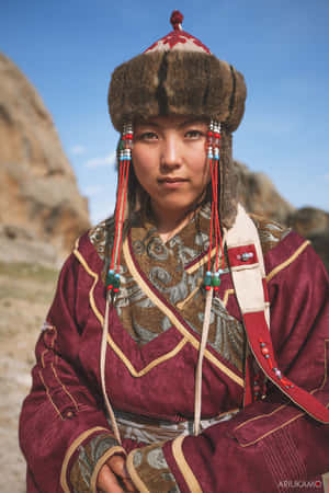 一位穿著傳統蒙古服裝的年輕女性，在岩石山景前擺姿勢。 — 亞洲 壁紙