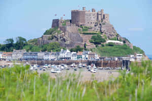 岩石島上的中世紀城堡俯瞰著擁有船隻和沿海建築的港口。 — 城堡 壁紙