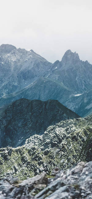 崎嶇的山峰在霧中升起，岩石前景。 — OnePlus 壁紙