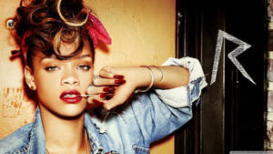 Rihanna 穿著牛仔外套，塗著紅色唇膏，手靠近臉部，站在塗鴉牆前。