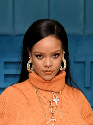 Rihanna 身穿橙色高領毛衣，搭配金色首飾和大圈耳環。