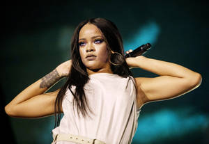 Rihanna 在舞台上手持麥克風，在藍色舞台燈光下表演。