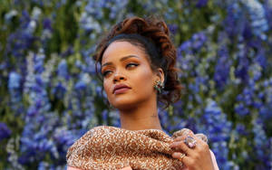 Rihanna 身穿棕色質感上衣，站在藍色花朵中，表情若有所思。