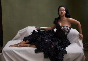 Rihanna 身穿黑色荷葉邊禮服，躺在一張白色垂簾沙發上。