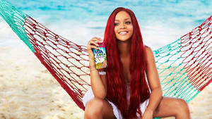 Rihanna 喺彩色吊床入面喺海灘上揸住椰子飲品。