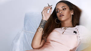 Rihanna 喺粉紅色連身裙入面挨住，揸住一支煙，身上有紋身同金飾。