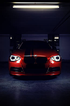 帶有黑色條紋的紅色BMW跑車，在螢光燈下的黑暗地下車庫中停放。
