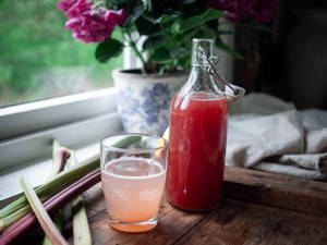 大黃飲料在玻璃杯和瓶子中，放在木窗台上，有粉紅色的花朵。 — Jugo GIF 壁紙