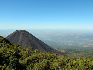 藍天下，前景是綠色森林，俯瞰朦朧山谷的火山