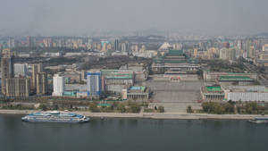 一條寬闊的河流上有一艘船，經過一個建築密集的城市，天空朦朧。