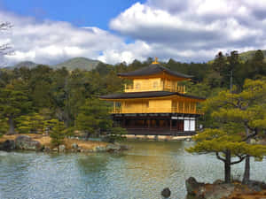 金色寺廟亭閣被水和綠樹環繞，天空多雲。 — 日本 壁紙