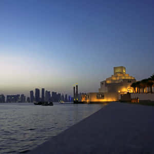 黃昏時分，一座燈火通明的博物館建築矗立在水邊，背景是城市天際線。 — 藍天 壁紙